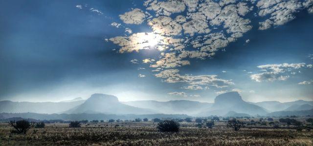 Smoke seen settling into a desert valley under a blue sky.