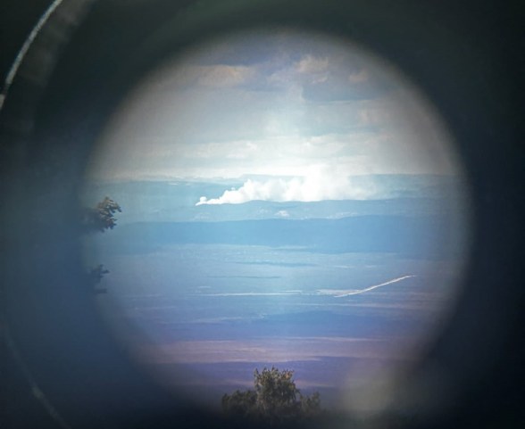 White smoke rises from a forest, as scene through a binocular lens.