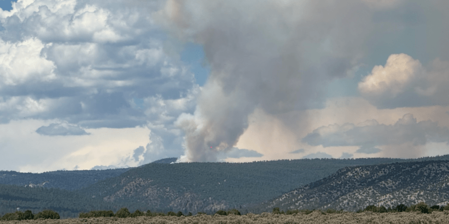Smoke rises from a forested mountainous area.